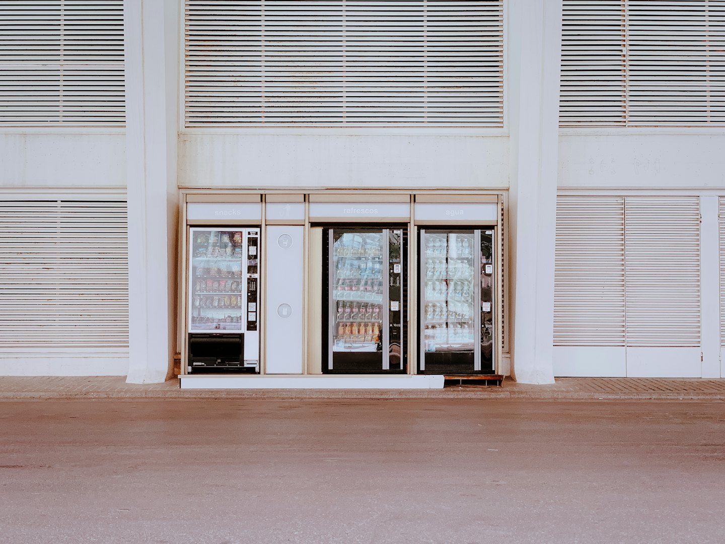 Three vending machines stand side by side against a slat wall.